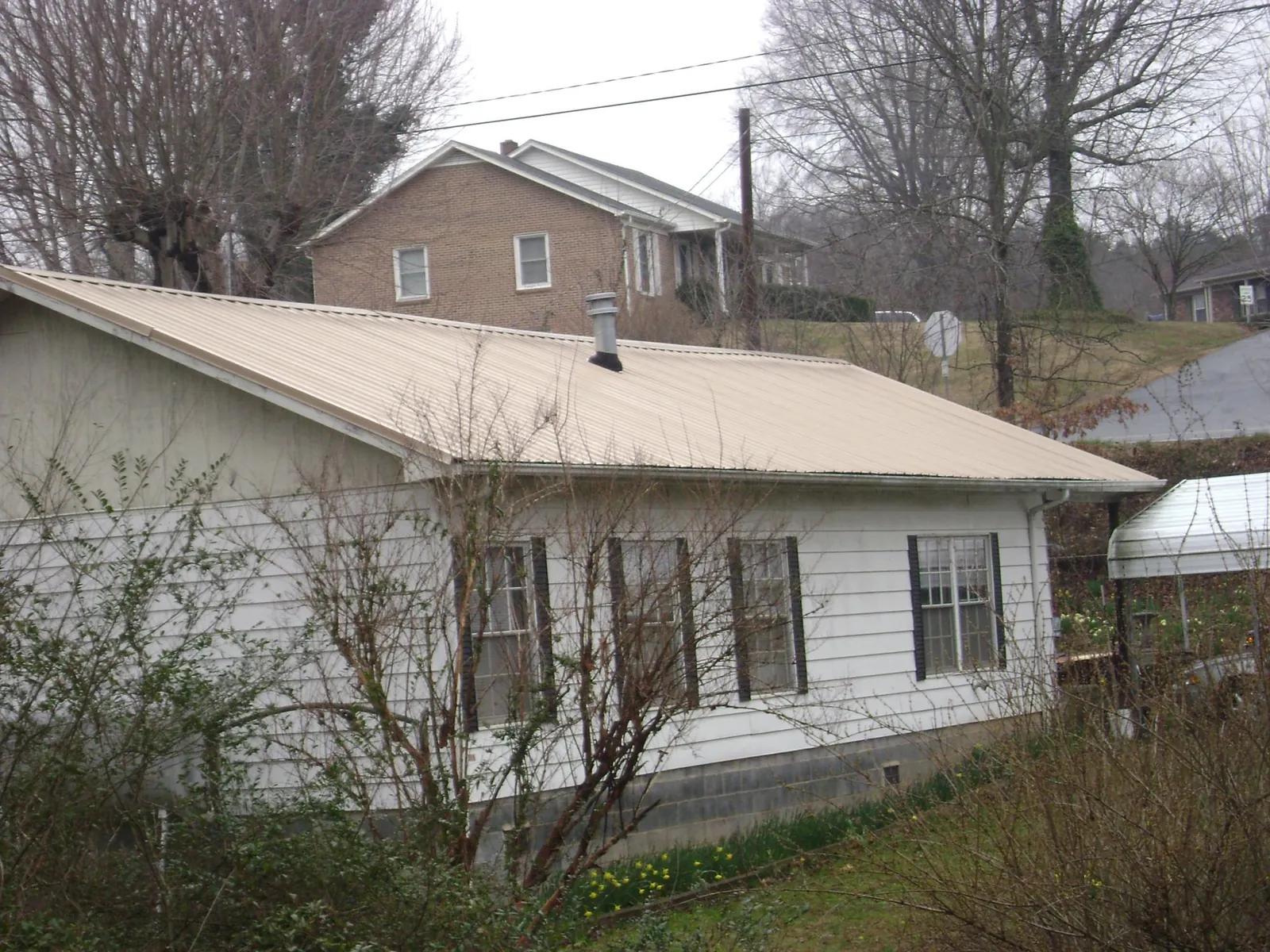 Tan metal roof on a white sided house set into a hillside — Commercial Roofing by Roofing Brothers in Campbelltown